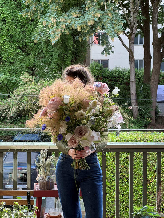 Grande seasonal bouquet with 25+ stems of smoke bush, blush roses, lisianthus and cornflowers, so large it hides the person holding it, by Kvetka Flower