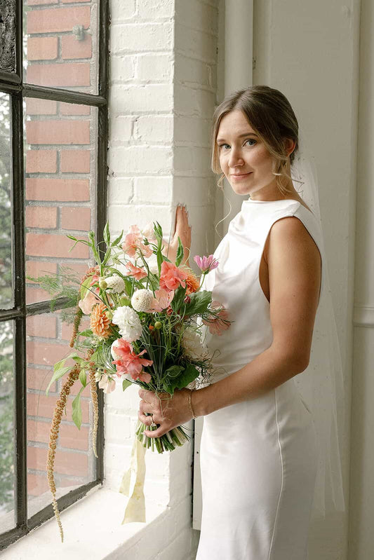 Bride standing near window with soft bridal bouquet at Tendue
