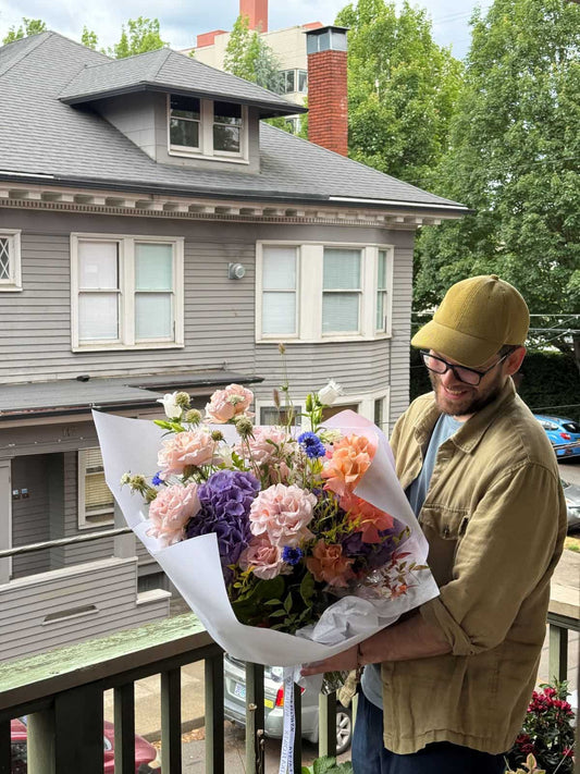 Happy customer holding a large fresh seasonal bouquet with garden roses, purple hydrangea and cornflowers on a porch, by Kvetka Flower