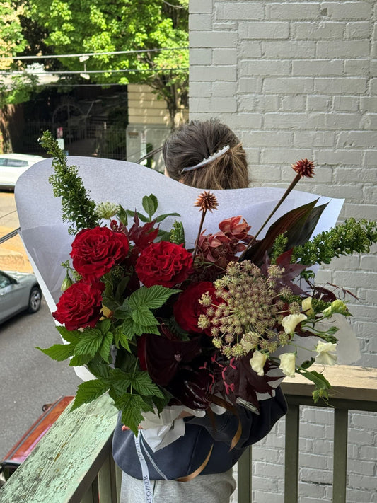 Fresh seasonal summer bouquet with red roses, orchids, anthurium, sweet pea, and raspberry greenery by Kvetka Flower