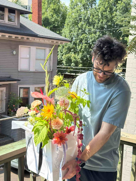 Florist holding a Fresh Seasonal Bouquet with sunflowers, garden roses, dahlias and amaranth in a Kvetka Flower bag before delivery in Austin, TX