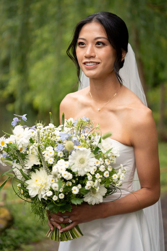 Bride smiling while holding a white and blue wedding bouquet by Kvetka Flower during vows