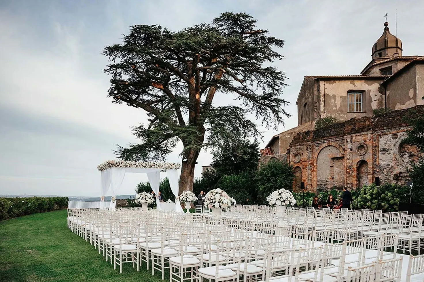 Outdoor wedding setup with white chairs and floral arrangements in front of an old building.