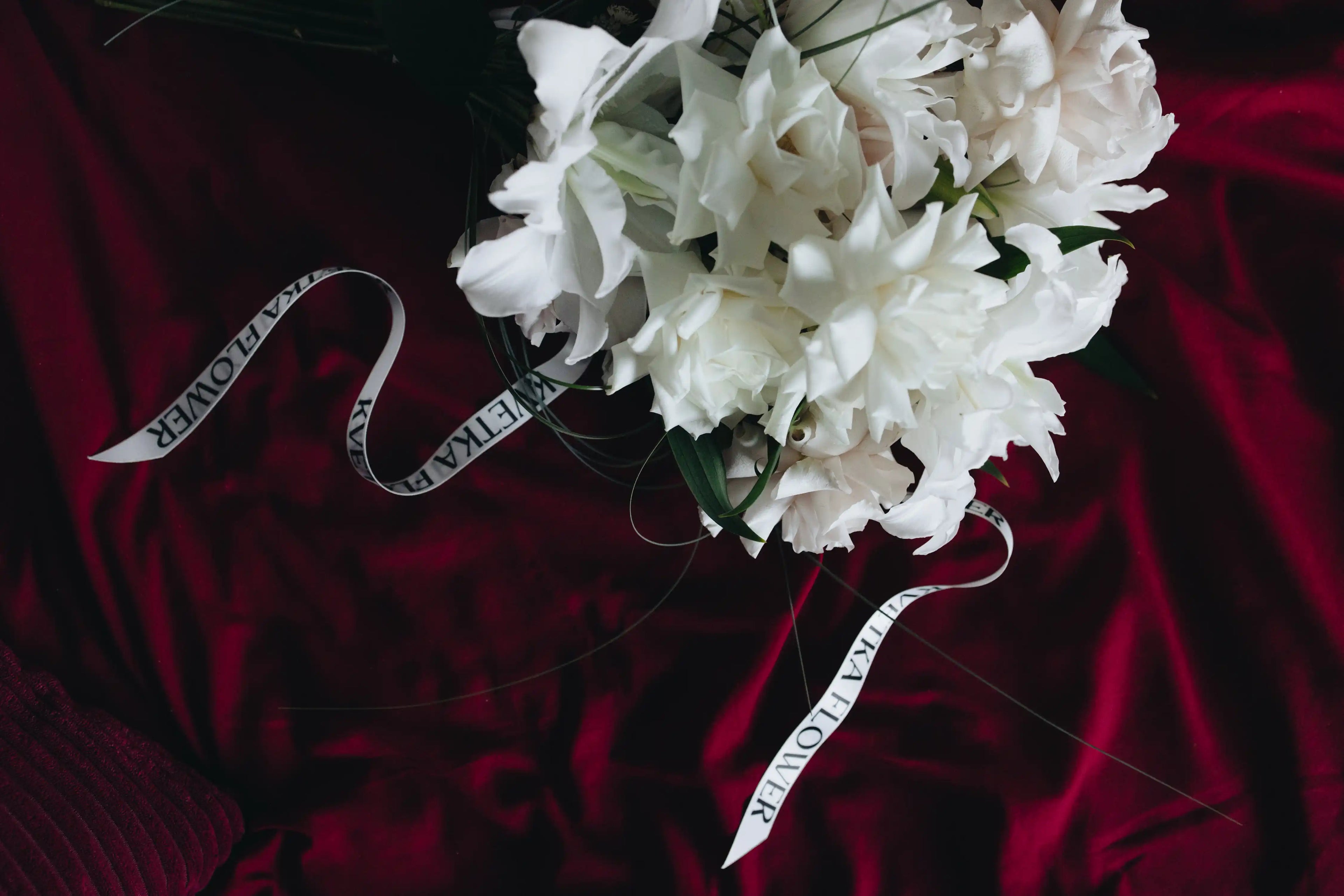 White bouquet made of local lilies with Kvetka Flower ribbon on a deep red background — luxury wedding flowers.
